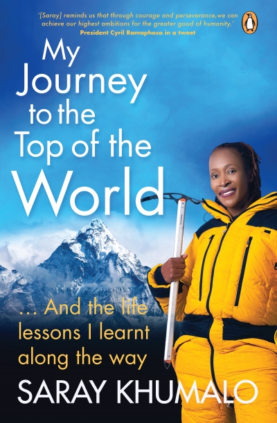 Author is in yellow snow suit holding an ice ax. In the background is Everest and a blue sky. 